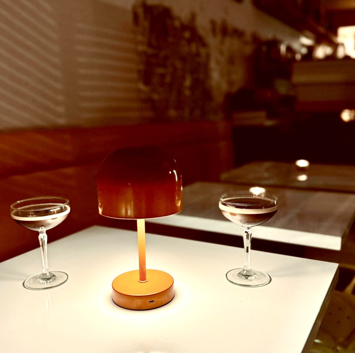 Two coupe glasses under a table lamp at an evening event