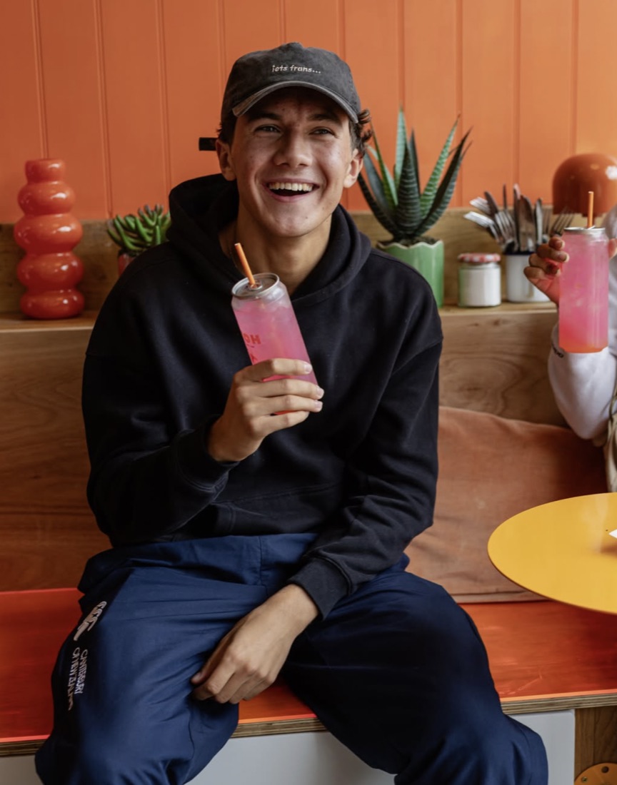 Customer laughing with a pink drink on the orange bench inside Kitch