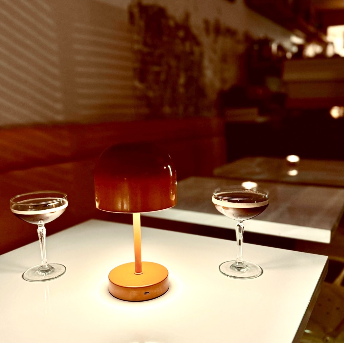 Two coupe glasses under a table lamp at an evening event